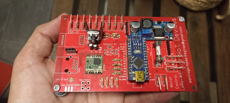 Custom red PCB held in hand showing Arduino Nano, RFM95 LoRa module, power regulation and relay connectors